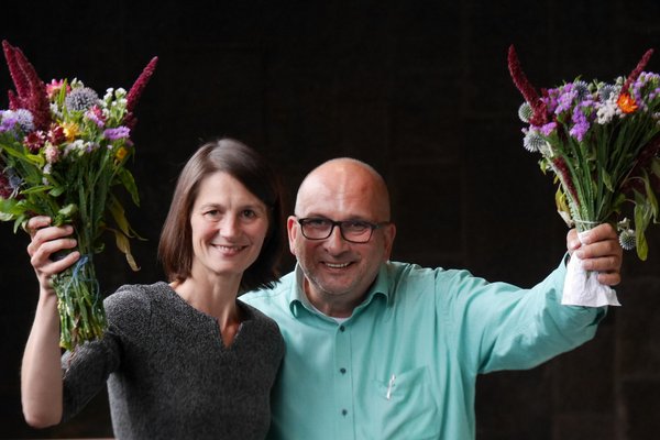 Miriam Staudte und Detlev Schulz-Hendel lächeln und schwenken Blumensträuße