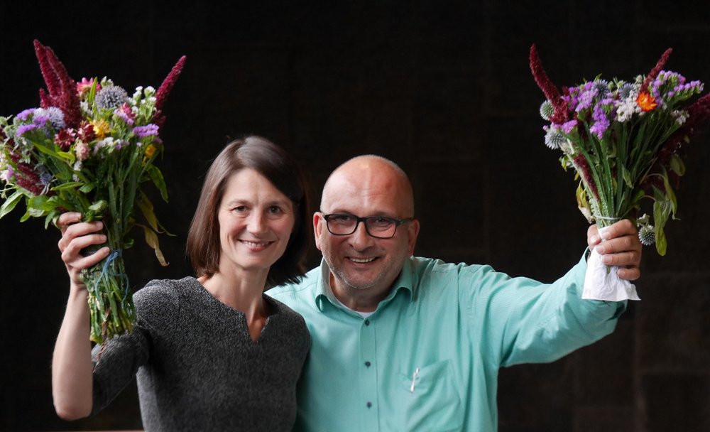 Miriam Staudte und Detlev Schulz-Hendel lächeln und schwenken Blumensträuße