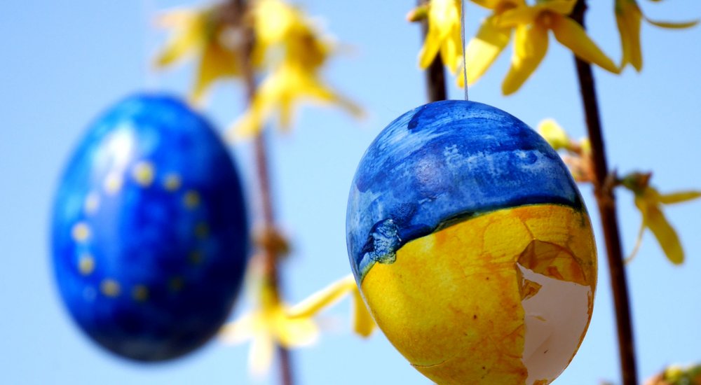 Beschädigtes Osterei in ukrainischen Nationalfarben vor Osterei in EU Farben