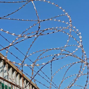 Maschendrahtzaun mit "NATO-Draht" und Überwachungskamera