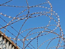 Maschendrahtzaun mit "NATO-Draht" und Überwachungskamera