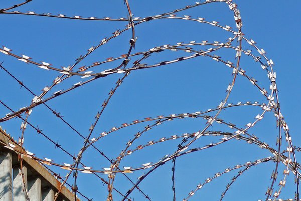 Maschendrahtzaun mit "NATO-Draht" und Überwachungskamera